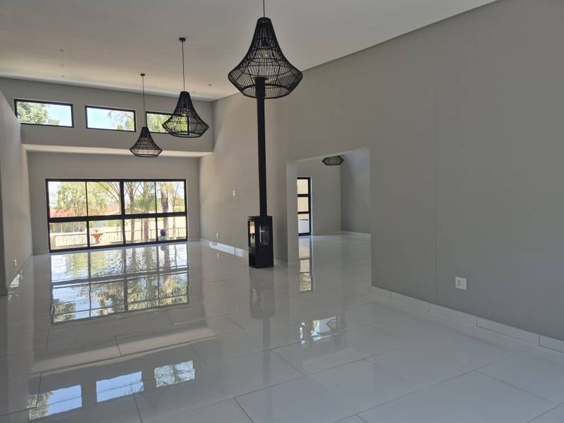 Spacious, modern open-plan living area featuring high ceilings, polished porcelain tile flooring, and a sleek freestanding fireplace with large glass sliding doors.