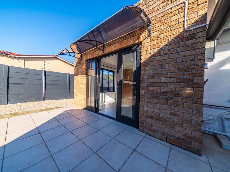 A clean, tiled patio area featuring a brick facade, modern sliding glass doors, and a protective polycarbonate awning.