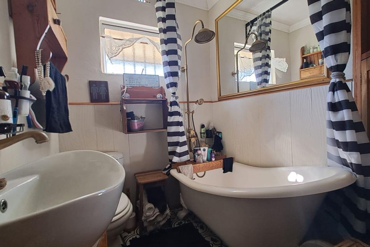 A compact bathroom featuring a freestanding bathtub with an exposed pipe shower mixer, a basin, toilet, and decorative patterned floor tiles.