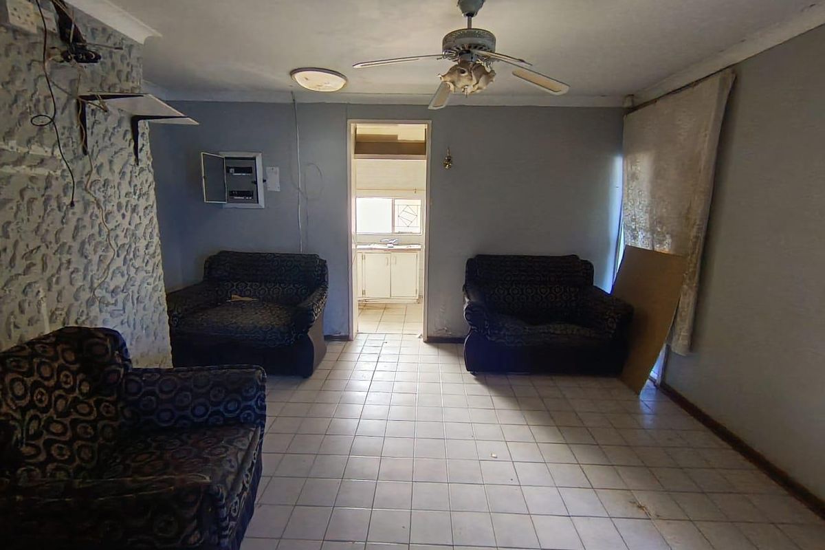 A living area featuring tiled flooring, a ceiling fan, and a textured feature wall, with direct access to an adjacent kitchen space.