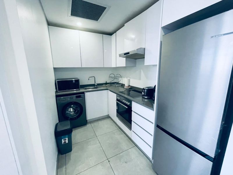 A compact, modern kitchen featuring white cabinetry, stone-look countertops, integrated appliances, and tiled flooring.