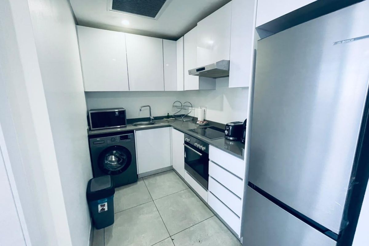 A compact, modern kitchen featuring white cabinetry, stone-look countertops, integrated appliances, and tiled flooring.