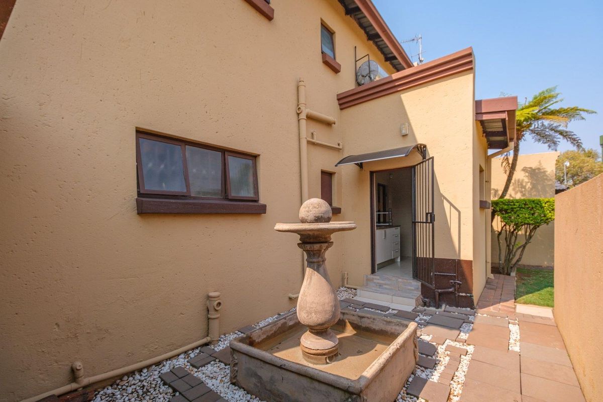 Rear exterior view featuring a stone fountain, paved walkway, and access to the home via a security gate and awning-covered entrance.