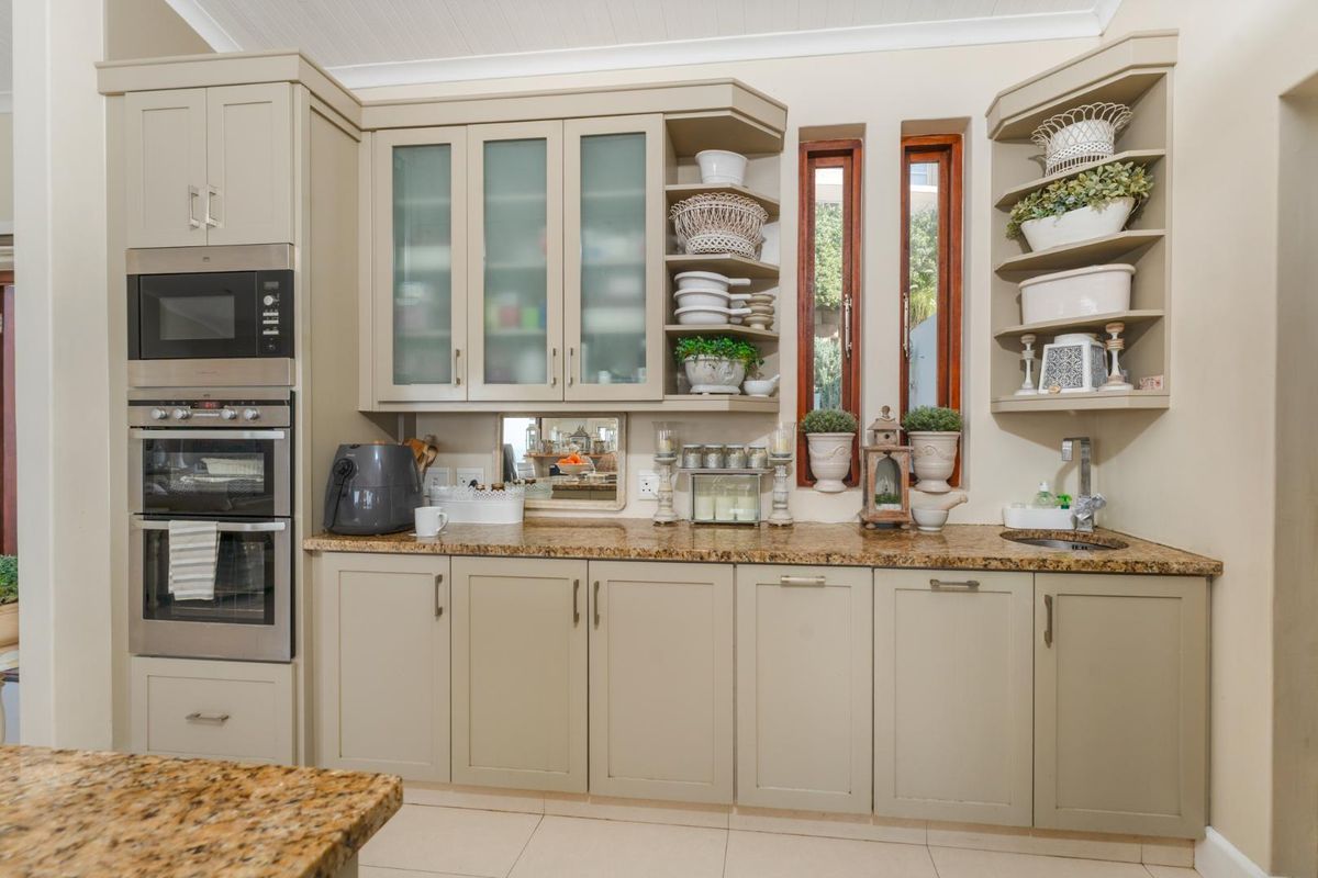 A well-maintained kitchen featuring granite countertops, built-in double oven, microwave, and ample shaker-style cabinetry with integrated shelving and a small prep sink.