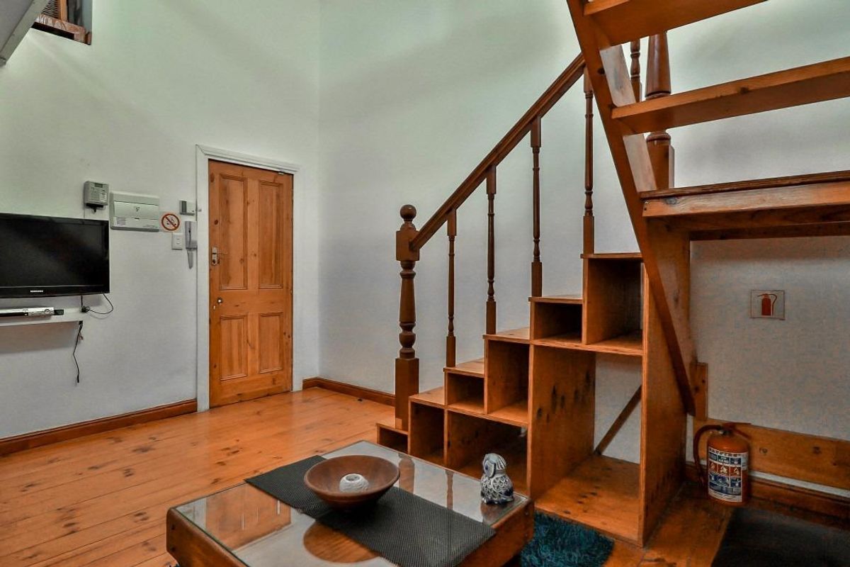 Living area featuring timber flooring and a built-in timber staircase with integrated storage, providing access to the upper level.