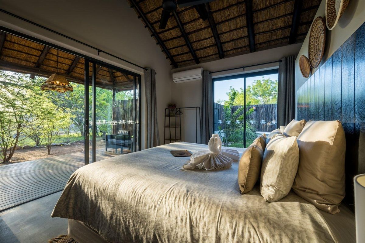 A well-appointed bedroom featuring a high thatched ceiling with exposed rafters, sliding glass doors opening onto a private timber deck, and integrated air conditioning.