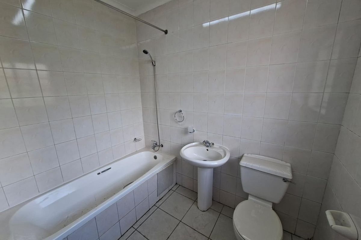 A dated bathroom featuring a standard bathtub with shower attachment, pedestal basin, and toilet, finished with full-height wall tiling.