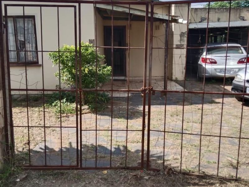 Front view of a residential property featuring a metal security gate, paved driveway, and an attached carport.