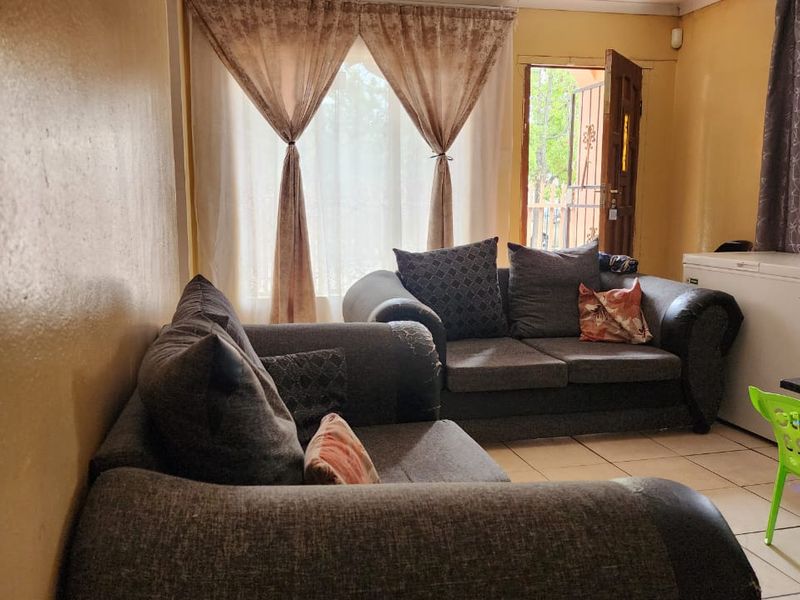 A living room area featuring tiled flooring and direct access to the exterior through a timber door with a security gate.