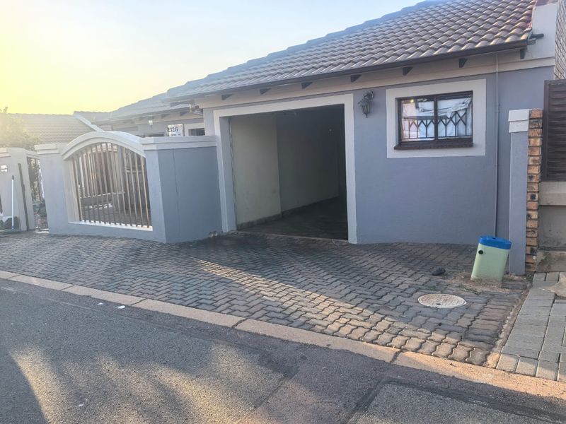 Front exterior view of the property featuring a paved driveway, a garage entrance, and a secure perimeter wall with a gate.