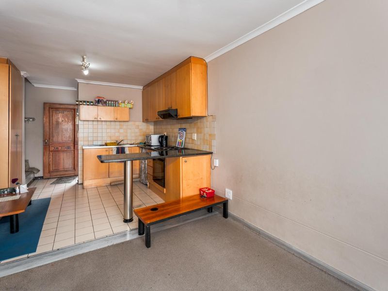 Open plan kitchen and living area featuring dated wooden cabinetry, a breakfast bar, tiled kitchen flooring, and carpeted living space.