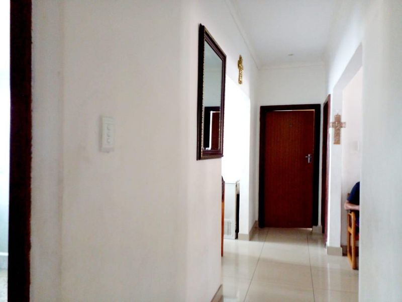 A clean and simple hallway featuring neutral white walls and tiled flooring, providing access to various rooms within the home.