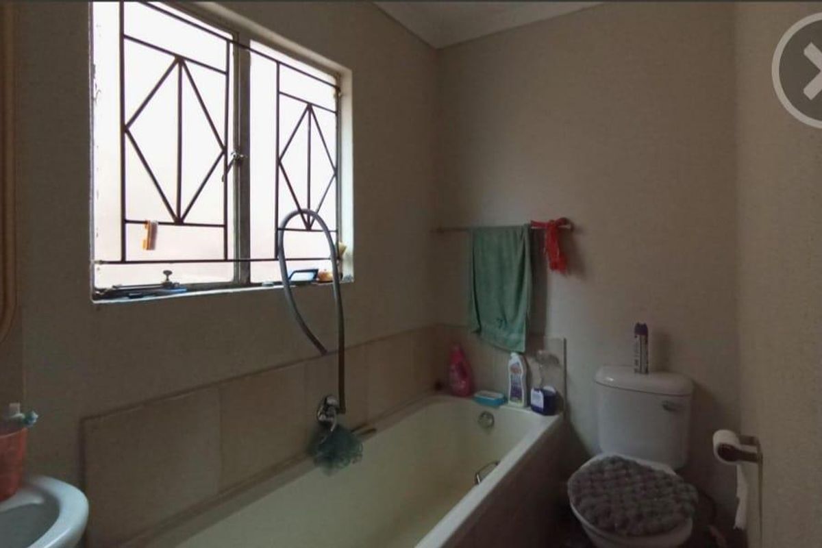 A functional bathroom featuring a built-in bathtub, standard toilet, and wall-mounted basin with security bars on the window.