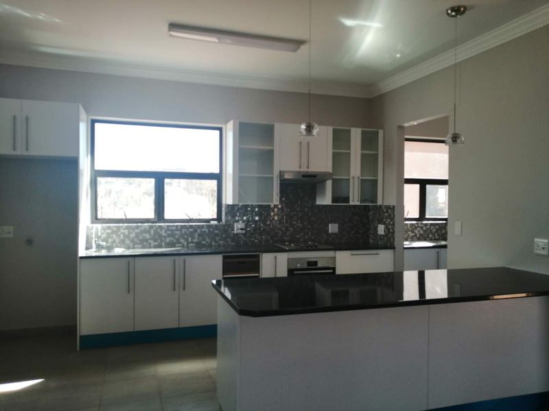 Modern kitchen featuring white cabinetry, dark granite countertops, mosaic tile backsplash, built-in oven, hob, extractor fan, and a central island with pendant lighting.