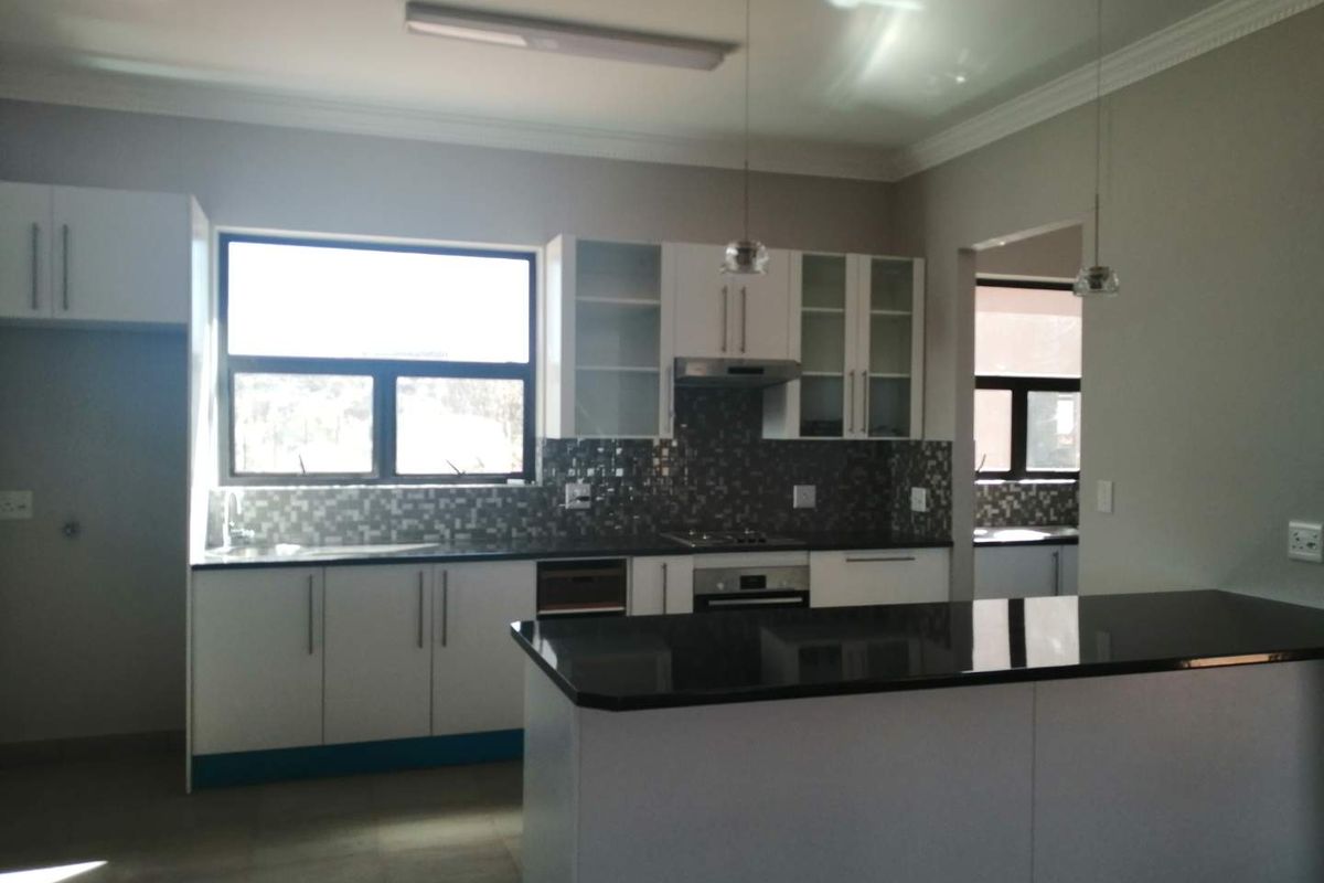Modern kitchen featuring white cabinetry, dark granite countertops, mosaic tile backsplash, built-in oven, hob, extractor fan, and a central island with pendant lighting.