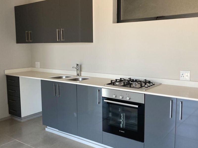 Modern kitchen featuring sleek grey cabinetry, stone countertops, a gas hob, and a built-in oven, offering a clean and functional workspace.