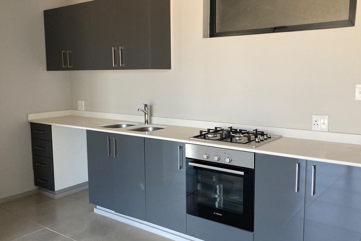 Modern kitchen featuring sleek grey cabinetry, stone countertops, a gas hob, and a built-in oven, offering a clean and functional workspace.