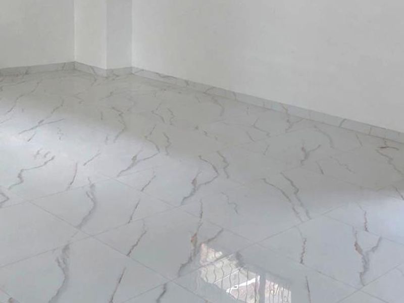 A bright, vacant office space featuring modern marble-effect tiled flooring and a window fitted with security bars.