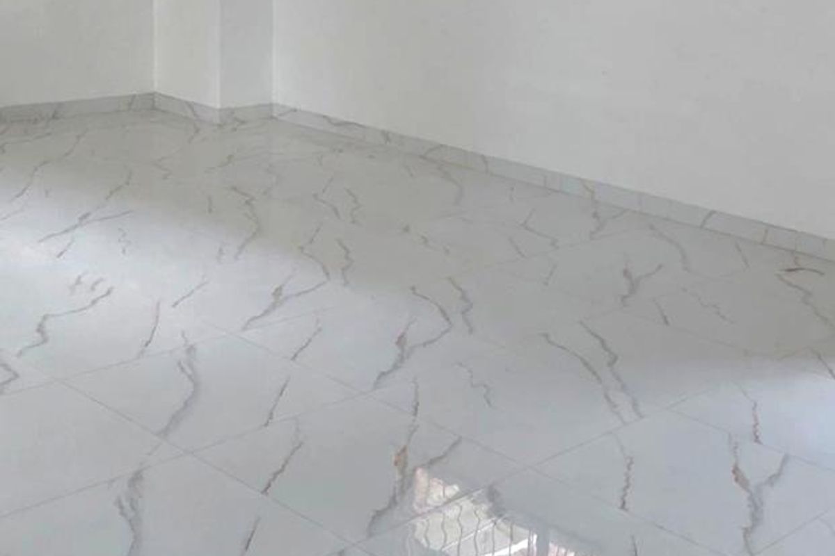 A bright, vacant office space featuring modern marble-effect tiled flooring and a window fitted with security bars.
