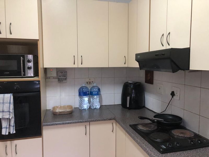 A functional kitchen featuring built-in cabinetry, a laminate countertop, tiled backsplash, and integrated appliances including an oven, hob, and extractor fan.