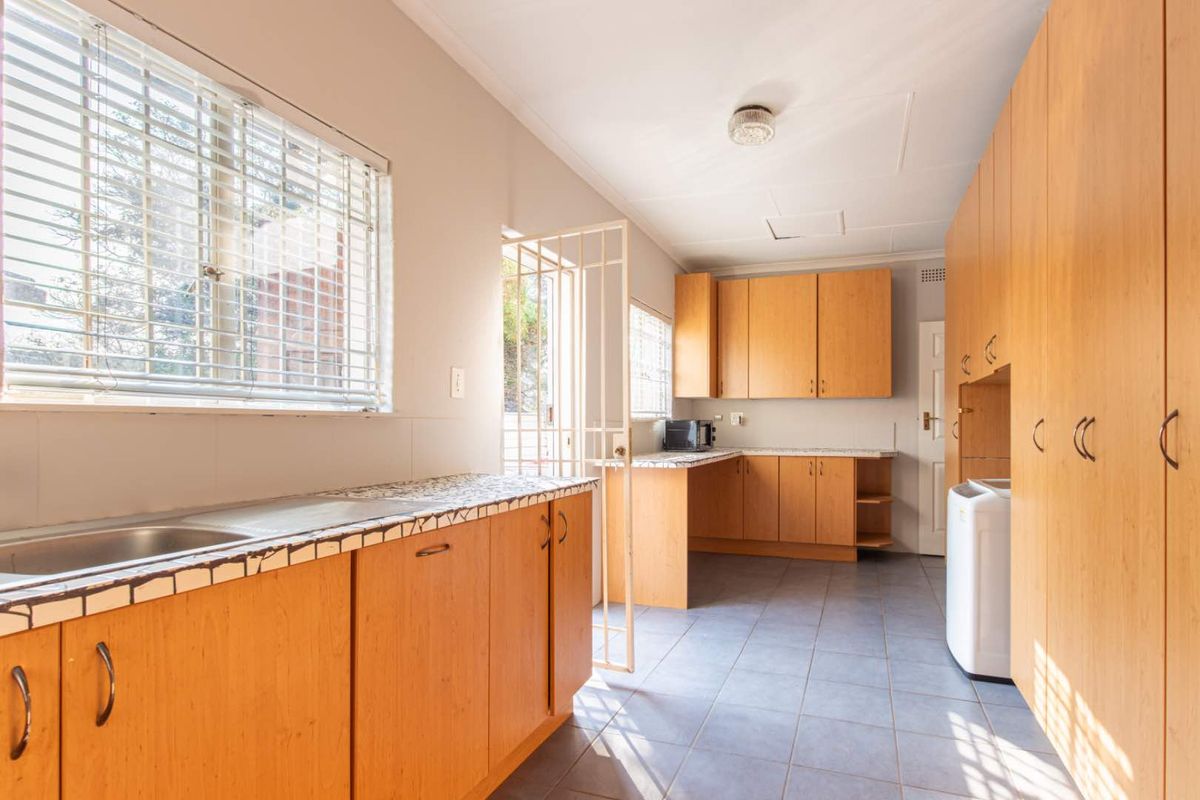 Functional kitchen featuring light wood cabinetry, tiled countertops, tiled flooring, and direct access to the exterior via a security gate.