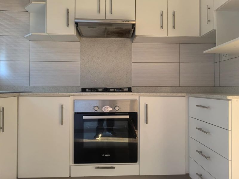 A clean, modern kitchen featuring white cabinetry, stone countertops, a tiled backsplash, and integrated Bosch oven with gas hob and extractor fan.