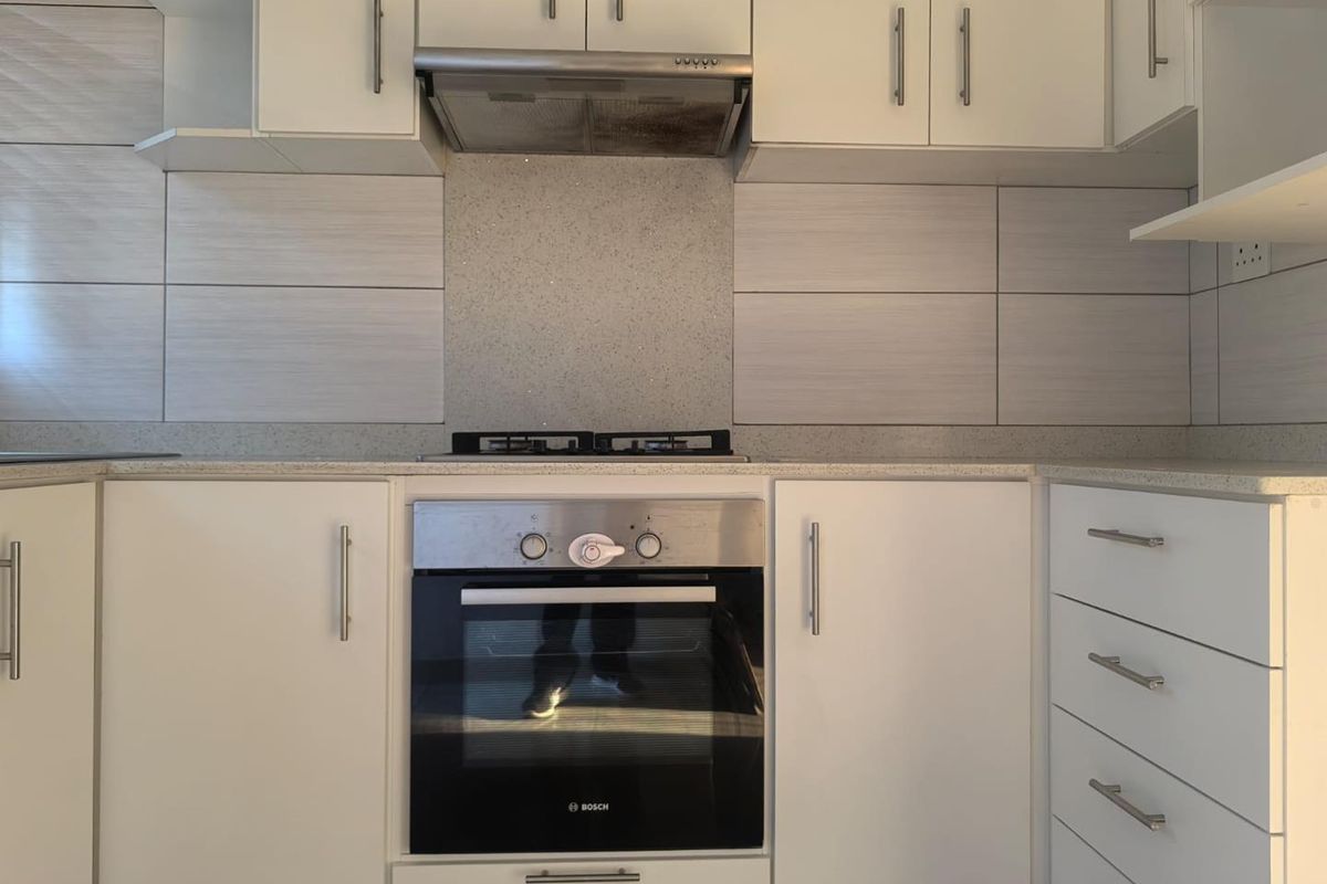 A clean, modern kitchen featuring white cabinetry, stone countertops, a tiled backsplash, and integrated Bosch oven with gas hob and extractor fan.