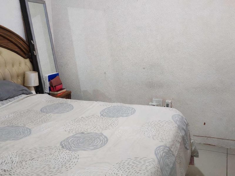 A bedroom featuring tiled flooring and standard electrical outlets, currently showing signs of wear on the wall surfaces.