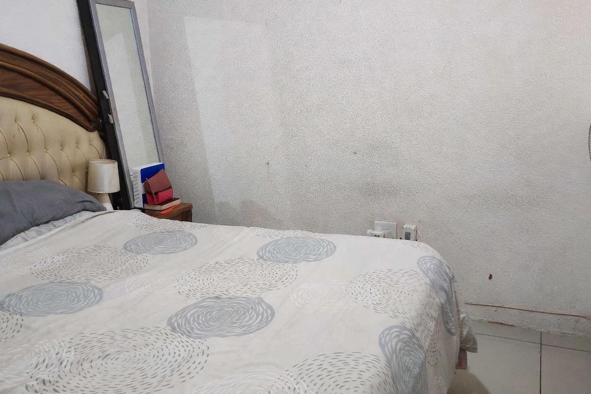 A bedroom featuring tiled flooring and standard electrical outlets, currently showing signs of wear on the wall surfaces.