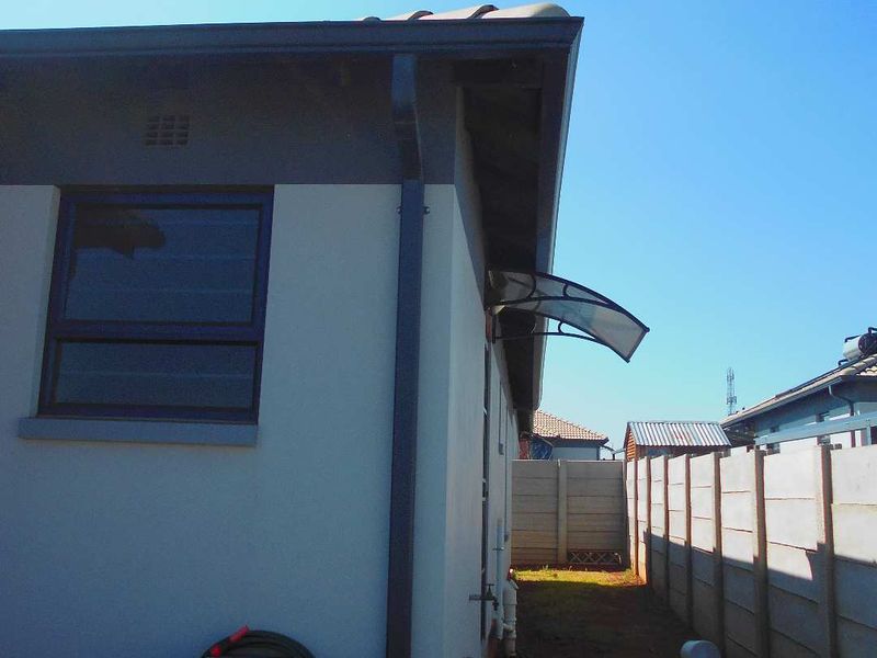 A view of the rear exterior side passage featuring a precast concrete boundary wall, tiled roof, and an installed window awning.