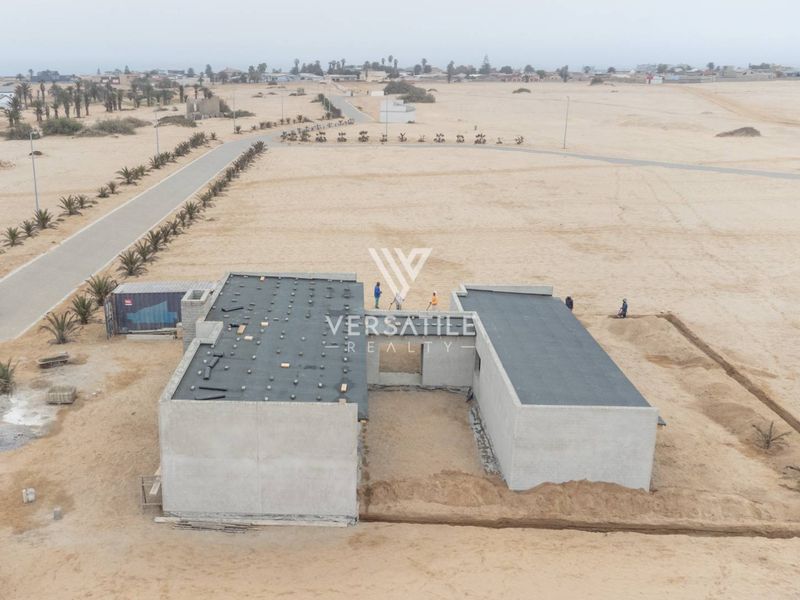 Aerial view of a residential property under construction, featuring a concrete shell structure with a flat roof in a desert landscape setting.