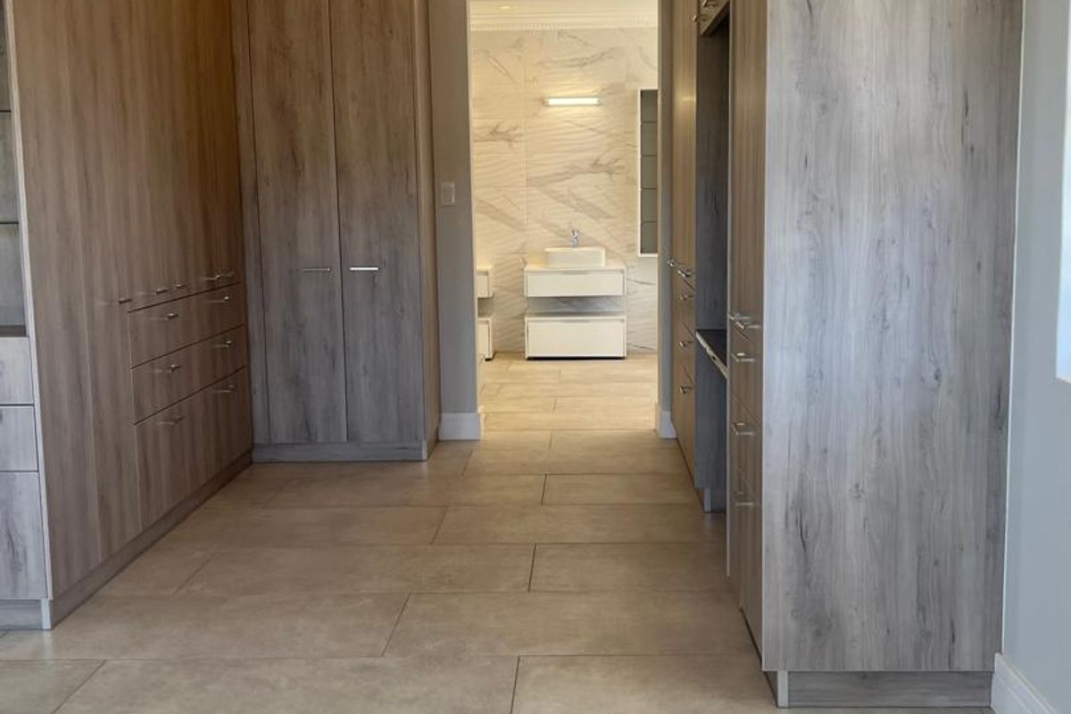 A spacious walk-in dressing area featuring extensive built-in cabinetry with wood-grain finish, leading into a modern bathroom with marble-style wall tiles.