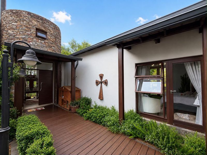 A well-maintained rear exterior featuring a stone-clad tower, timber decking, and covered walkway providing access to the home's interior living spaces.