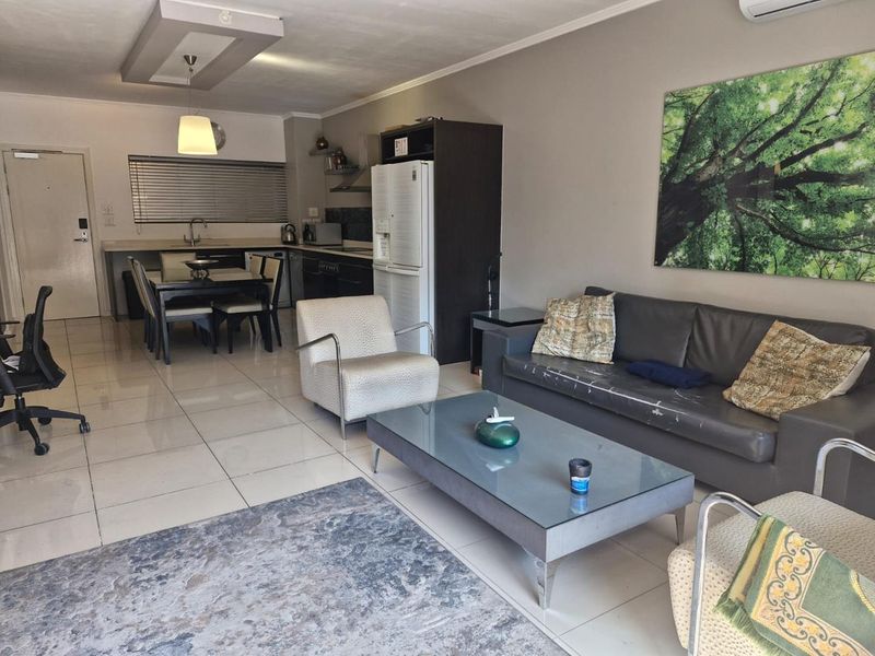 Open-plan living and kitchen area featuring tiled floors, modern recessed ceiling lighting, and a functional kitchen layout with built-in cabinetry and appliances.
