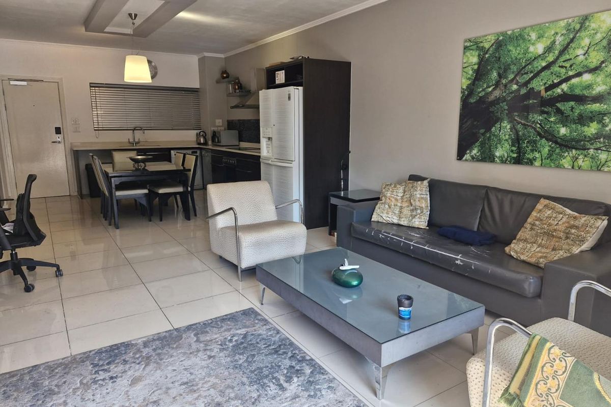 Open-plan living and kitchen area featuring tiled floors, modern recessed ceiling lighting, and a functional kitchen layout with built-in cabinetry and appliances.