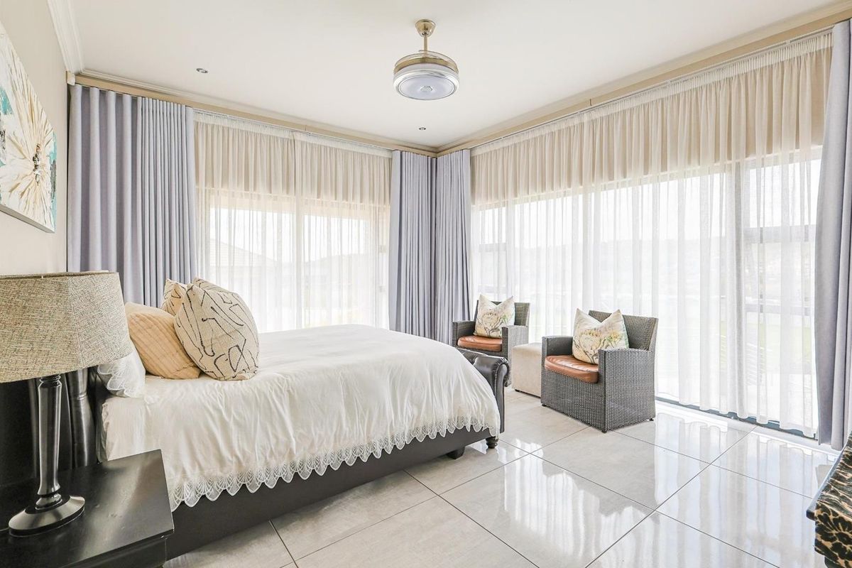 Spacious bedroom featuring large floor-to-ceiling windows with elegant curtains, polished tile flooring, and a modern ceiling fan.