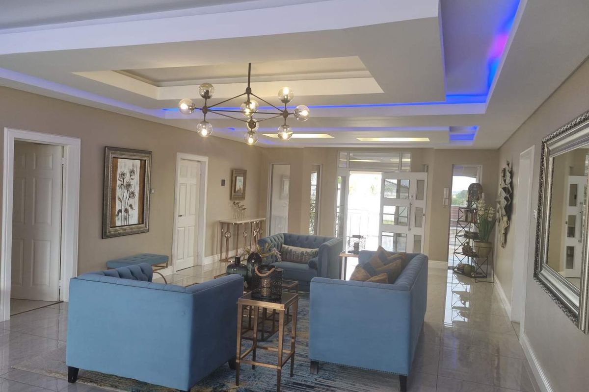 Spacious living room featuring a modern tray ceiling with integrated LED accent lighting, polished tile flooring, and a contemporary chandelier.