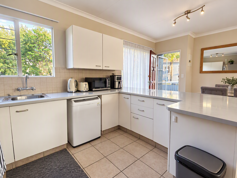 A functional kitchen featuring white cabinetry, tiled backsplash, and a breakfast bar, with direct access to an outdoor area.