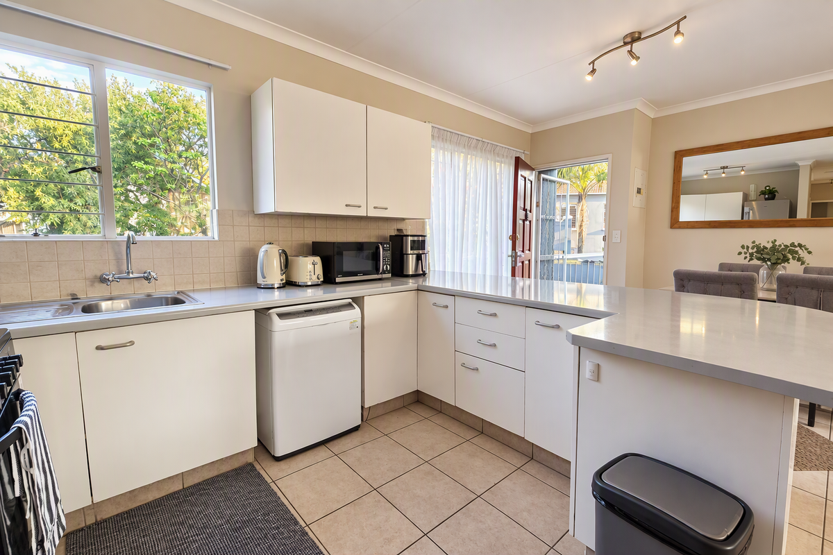 A functional kitchen featuring white cabinetry, tiled backsplash, and a breakfast bar, with direct access to an outdoor area.