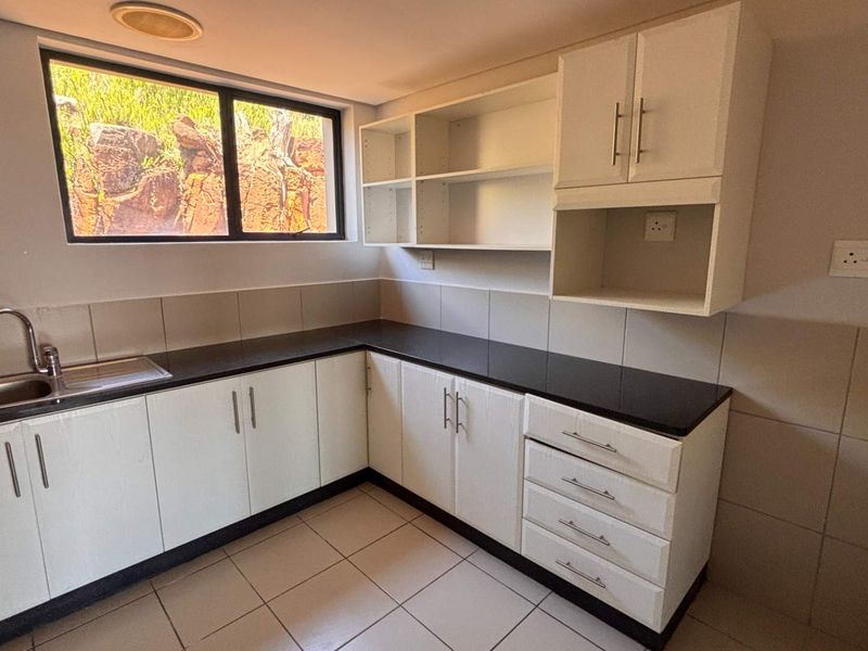 A clean, functional kitchen area featuring white built-in cabinetry, dark granite countertops, a stainless steel sink, and tiled finishes throughout.
