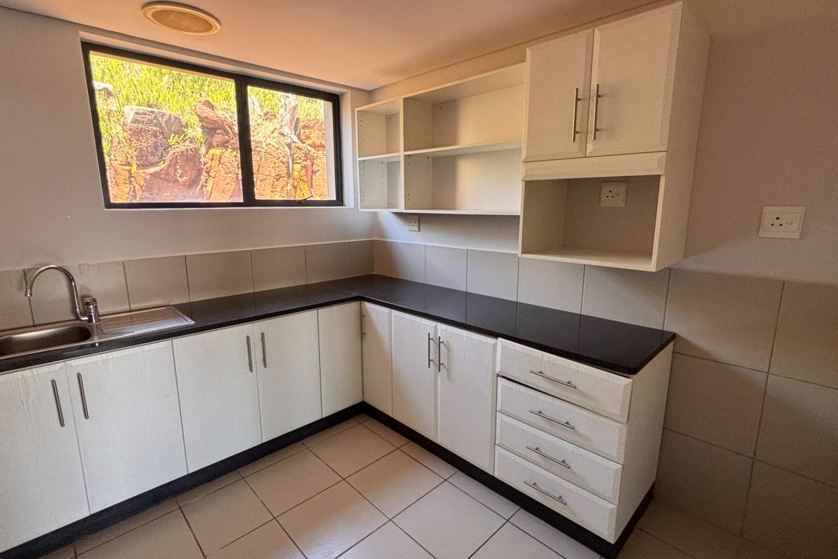 A clean, functional kitchen area featuring white built-in cabinetry, dark granite countertops, a stainless steel sink, and tiled finishes throughout.