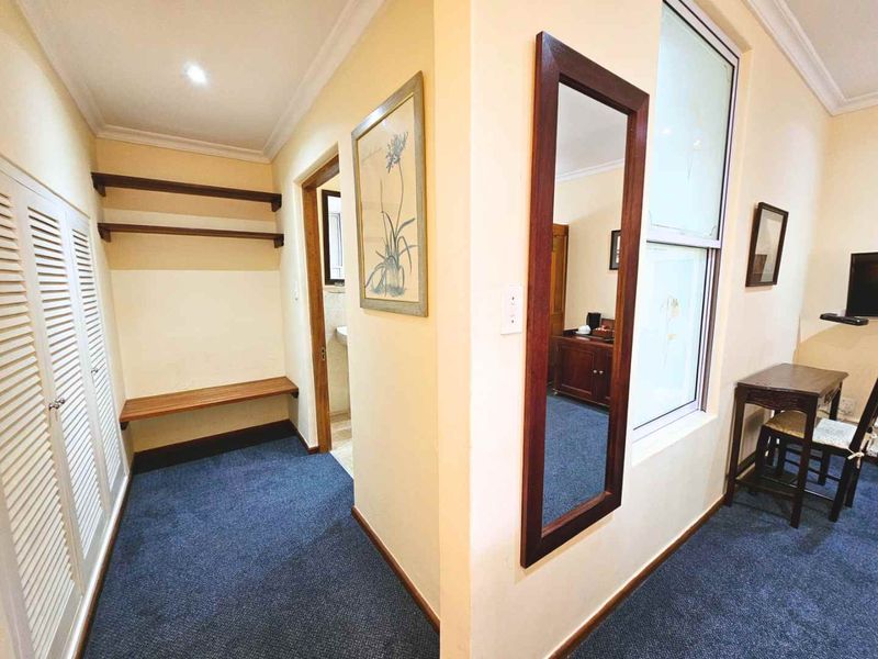 A functional hallway featuring built-in storage cupboards, carpeted flooring, and recessed ceiling lighting, providing access to adjacent rooms.