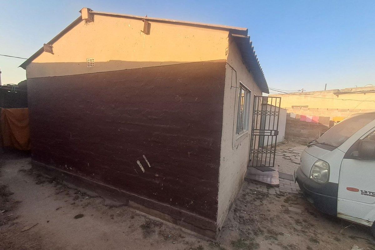 Rear view of the property showing the exterior wall, security gate, and corrugated roof structure.