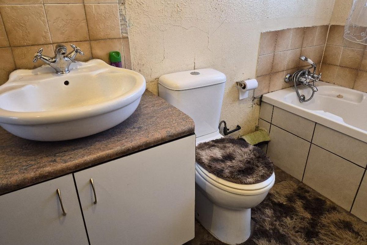 A dated bathroom featuring a vanity with basin, a standard toilet, and a tiled bathtub with shower mixer.