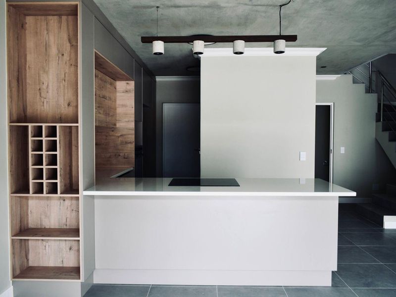 Modern kitchen featuring a central island with an induction cooktop, sleek cabinetry with integrated wine storage, and a contemporary staircase in the background.