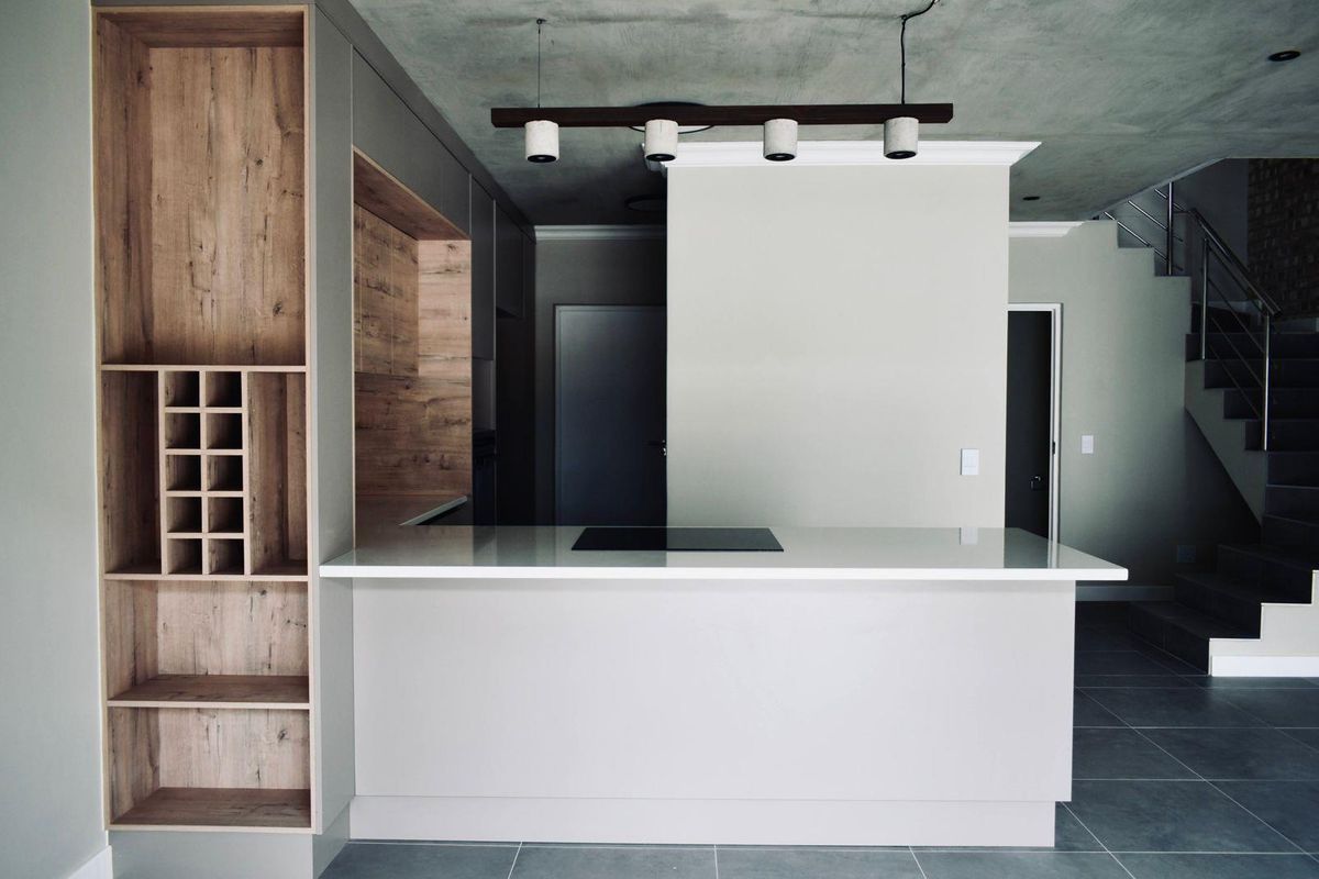 Modern kitchen featuring a central island with an induction cooktop, sleek cabinetry with integrated wine storage, and a contemporary staircase in the background.