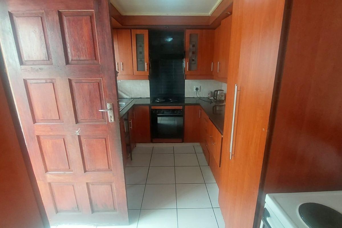 A compact kitchen featuring wooden cabinetry, built-in oven, hob, and tiled flooring, offering a functional layout for meal preparation.