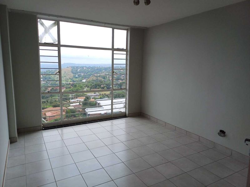An empty living room featuring large steel-framed windows with expansive views, ceramic tiled flooring, and neutral walls, ready for renovation or staging.