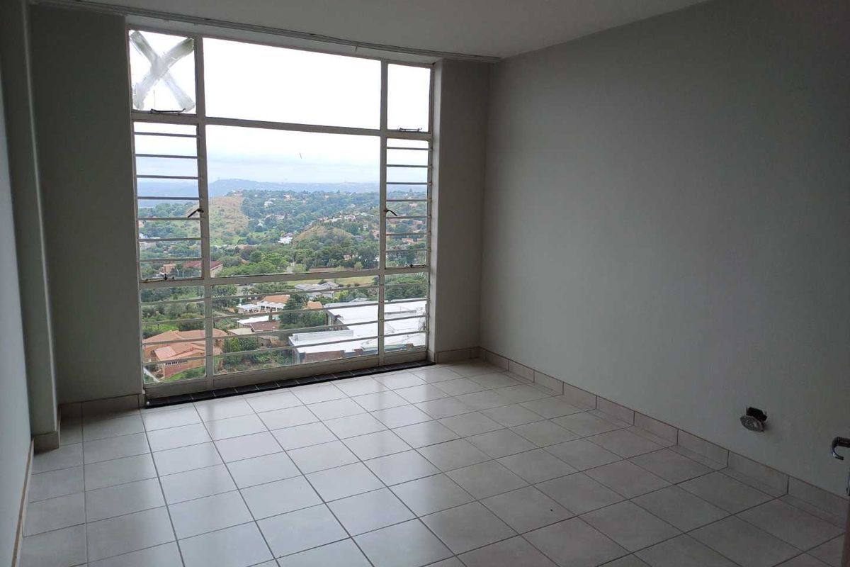 An empty living room featuring large steel-framed windows with expansive views, ceramic tiled flooring, and neutral walls, ready for renovation or staging.