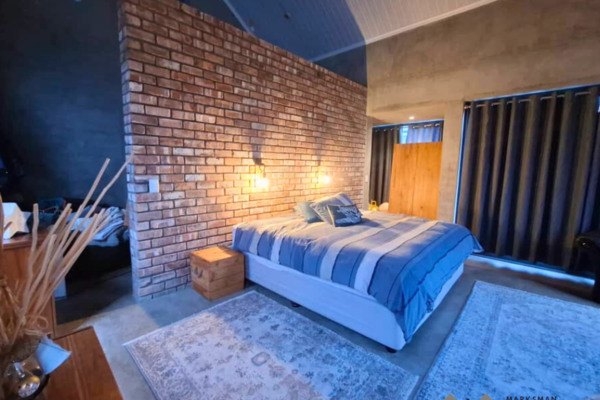 Spacious bedroom featuring a prominent exposed brick feature wall, high vaulted ceilings, and polished concrete flooring.